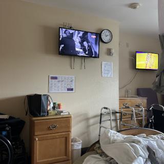 A view of a hospital room featuring a patient bed, two televisions, and various medical items.