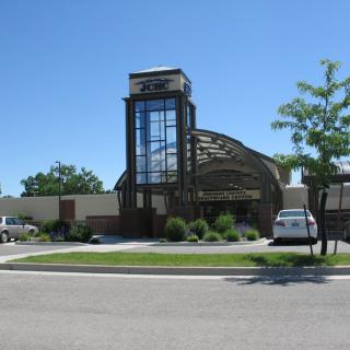 A modern building with a prominent glass feature and adjacent parking lot on a clear day.
