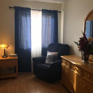 Cozy bedroom corner with a comfortable chair and wooden dresser near the window.