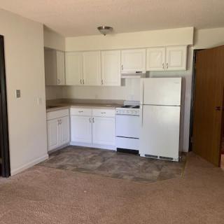 An empty apartment kitchen with white cabinets and appliances.