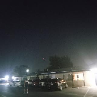 A quiet night at a roadside motel, illuminated by the faint glow of streetlights and surrounded by parked cars.