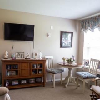 A cozy living room with a wall-mounted television, a wooden cabinet, and a small dining area by the window.