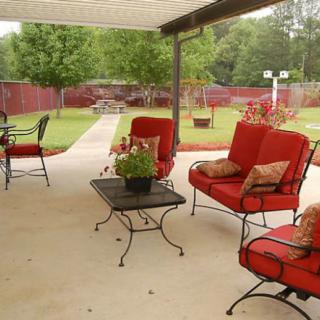 A cozy patio with red cushioned chairs and a table, set in a spacious backyard garden.