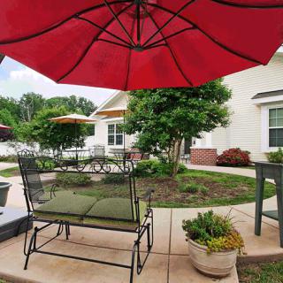 A cozy patio area featuring a red umbrella, lush greenery, and comfortable outdoor seating.