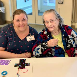 A caregiver and an elderly woman smiling together during a crafting session.