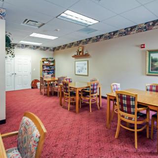 A cozy dining area with multiple tables and chairs, featuring a warm carpet and decorative lighting.