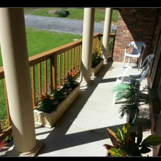 A sunny porch with columns, railings, and decorative plants.