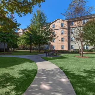 A sunny outdoor view of an apartment building with a landscaped pathway and trees.