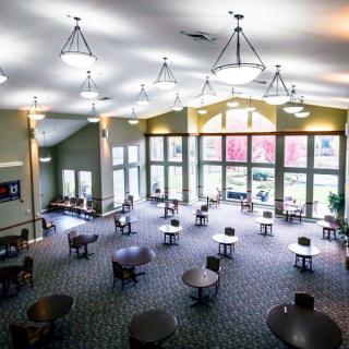 A spacious lobby with large windows, tables, and chairs under bright lighting.