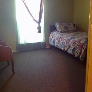 A simple bedroom with a single bed and chair beside a curtained window.