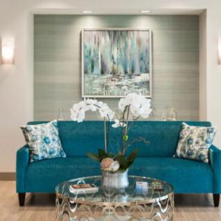 A modern living room with a turquoise sofa, floral cushions, and an orchid centerpiece on a glass coffee table.