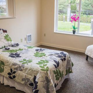 A simple and cozy bedroom with a single bed, floral bedding, a window view, and a flower vase on the sill.