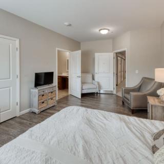 A modern bedroom featuring a TV, comfortable seating, and wooden flooring.