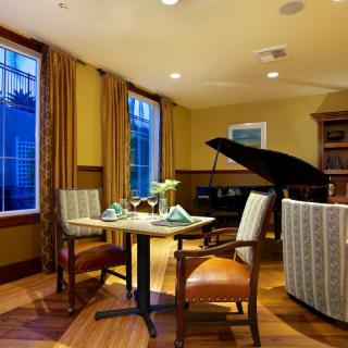 An elegant dining room featuring a grand piano and a cozy table setting by the window.