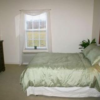 A cozy bedroom with a neatly made bed, a window with curtains, and a plant next to the bed.