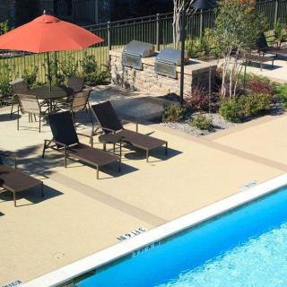 A sunny outdoor area featuring a swimming pool, lounge chairs, and a patio with an umbrella.
