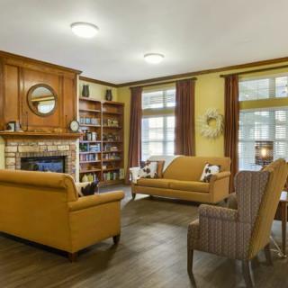 A cozy living room with warm tones, featuring sofas, an armchair, a fireplace, and a bookshelf.