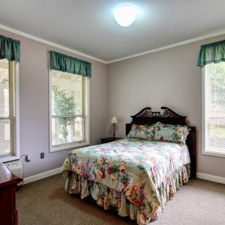 A cozy bedroom featuring a floral bedspread, two windows with valances, and a small bedside lamp.