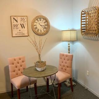 A cozy living room corner with two tufted pink chairs, a small round table, and decorative elements including a clock and a lamp.