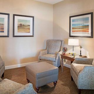 A cozy living room with armchairs, an ottoman, and framed artwork on the walls.
