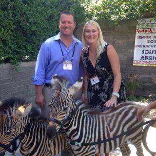 A smiling couple poses with zebras in an outdoor setting.