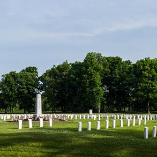 A serene view of a cemetery, with rows of grave markers and a memorial statue surrounded by lush greenery.