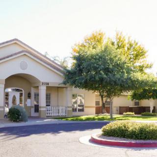 A sunny view of a building entrance with surrounding trees and a driveway.