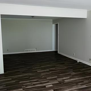 A minimalist, spacious room with a hardwood floor and white walls.