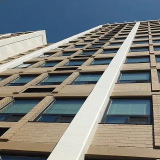 A modern high-rise building with a focus on its windows and facade, set against a clear blue sky.