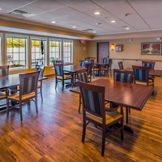 A spacious dining area with wooden tables and chairs, featuring large windows and a well-lit atmosphere.
