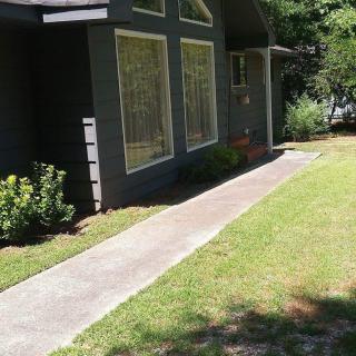 A view of a house exterior with large windows, a grassy yard, and a concrete pathway.