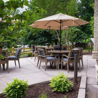 A serene patio setting with outdoor furniture and umbrella, surrounded by lush greenery.