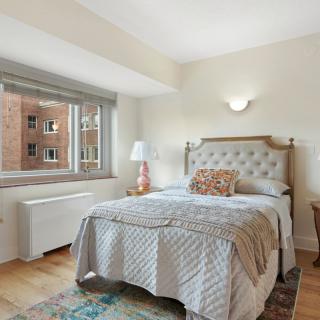A bright and cozy bedroom with a neatly made bed, large window, and stylish decor.
