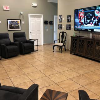 A waiting room with comfortable seating and a large television displaying a sports game.