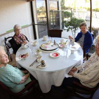 A group of elderly individuals enjoying a meal together around a table with a cake in the center.