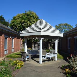 A shady gazebo surrounded by a garden area between two brick buildings.