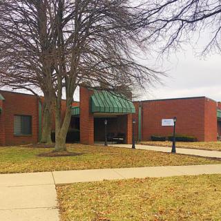 A brick building with a green awning and bare trees on a cloudy day.