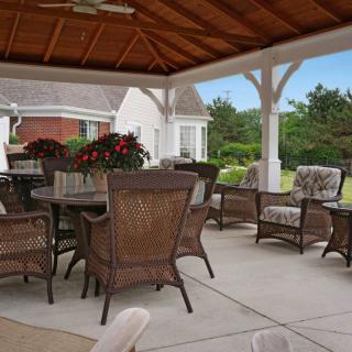 A cozy outdoor patio with wicker furniture under a gazebo, surrounded by lush greenery.