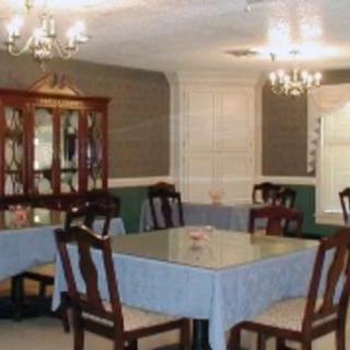 A traditional dining room with a central table, surrounded by chairs and illuminated by chandeliers.