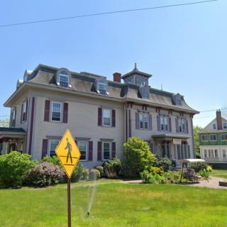 A historic residential building with a well-maintained lawn and a pedestrian crossing sign in the foreground.