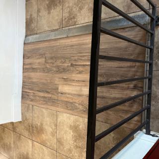 A close-up view of a modern interior featuring wood-like tiles and a sleek metal railing.