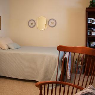 A cozy and well-decorated bedroom featuring a bed, rocking chair, and bookcase.