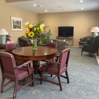 A cozy living room with a round table adorned with flowers, surrounded by chairs, and a TV in the corner.