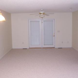 An empty room with carpet flooring, a ceiling fan, and French doors leading outside.