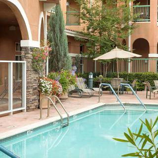A tranquil outdoor pool area with lounge chairs and an umbrella, surrounded by lush greenery.