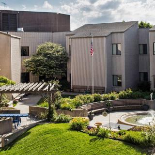 A modern building surrounded by a landscaped garden with trees and a flagpole.