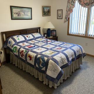 A cozy bedroom featuring a quilt-covered bed, art on the walls, and a window with curtains.