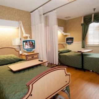 A hospital room with two patient beds separated by curtains, each equipped with a television.