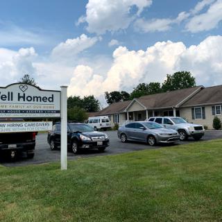 A view of a residential building with parked vehicles and a sign indicating its name.
