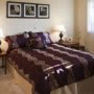 A cozy bedroom featuring a neatly made bed with a striped comforter, flanked by lamps and decorated with framed photographs on the wall.